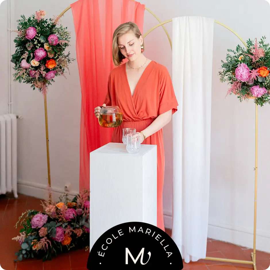 Formation Wedding Officiant : Une femme en robe orange se tient devant une table blanche, agissant en tant qu'officiante de mariage.
