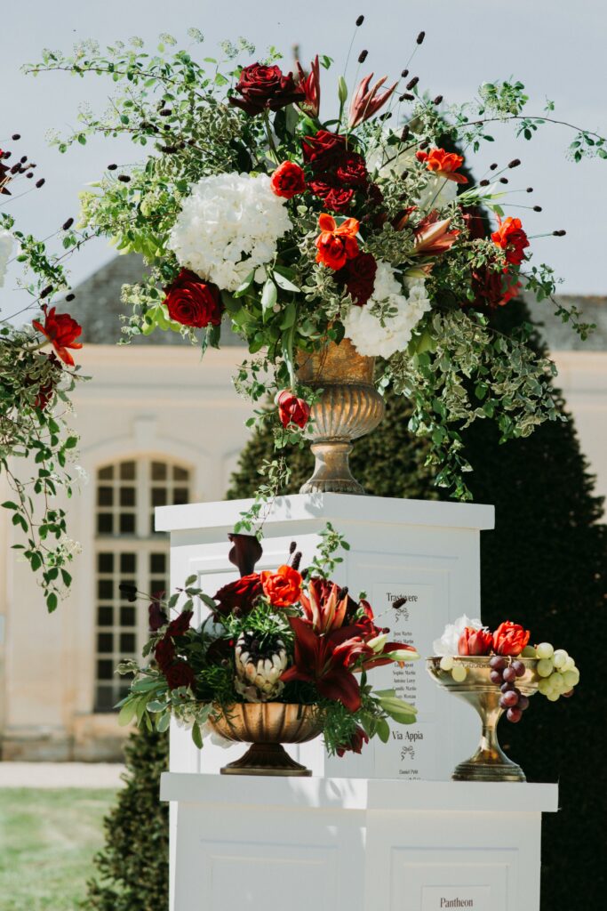 Plan de table sur colonnes blanches et compositions florales rouges et blanches pour un mariage à l’italienne au Château du Boschet